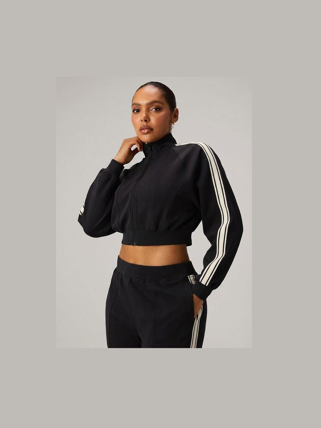Fabletics women's black cropped full-zip track jacket with mock neck, boxy fit, and white striped sleeve taping